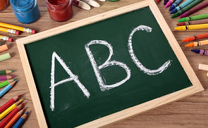 ABC written on a small elementary blackboard with various paints, crayons and pencils on a school desk.