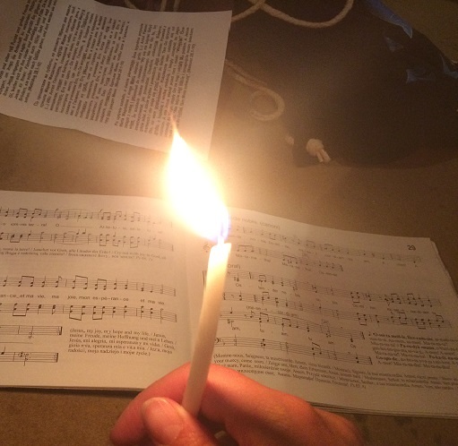 Hand hält Kerze vor einem Liederbuch