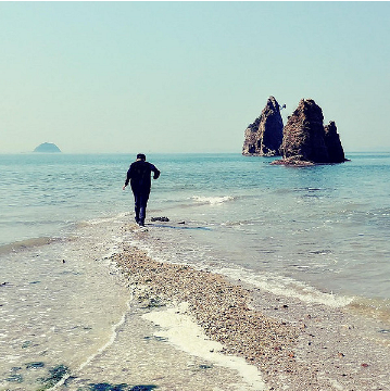 Mann geht am Strand in Richtung Felsen