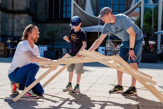 Bauen mit dem Dombaumeister; Lange Nacht der Kirchen 2026 / © Diözese Linz / Johannes Kienberger Kreativ-Workshops für Kinder: Dombaumeister Michael Hager (links im Bild) baute mit den Kindern Konstruktionen aus Holzstangen und Spielsteinen.