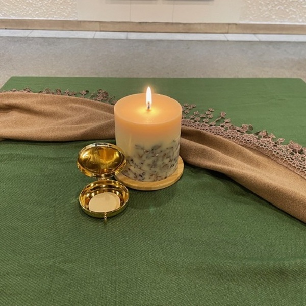 brennende Kerze mit Hostie in Pyxis auf grünem Tuch