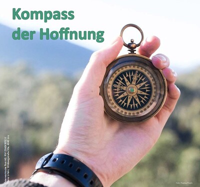 Eine Hand hält einen Kompass in die Höhe, im Hintergrund verschwommen ein Berg