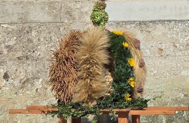 Erntedankkrone aus Getreide und Blumen vor steinerner Mauer