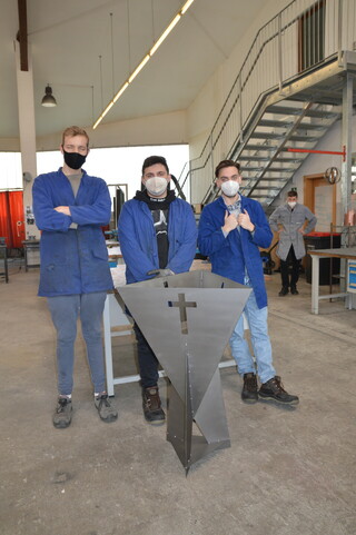Drei Arbeiter in der Produktionsschule mit der neu hergestellten Feuerschale 