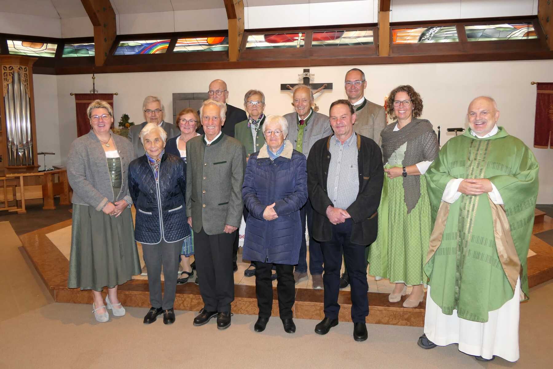 Gruppe von zwölf Personen in Tracht und Geistlichen Gewand vor einem Kreuz in einer Kirche.