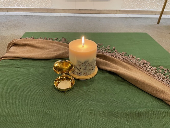 brennende Kerze mit Hostie in Pyxis auf grünem Tuch