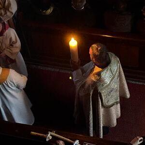 Diakon Julian Gillesberger bringt die Osterkerze in die dunkle Kirche