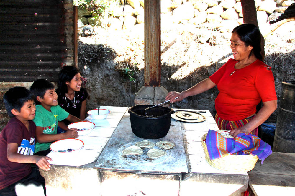 Eine Frau aus Guatemala kocht am neuen Energiesparofen und 3 Kinder schauen zu