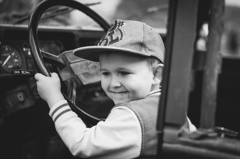 Kind am Fahrersitz eines Autos mit dem Lenkrad in den Händen