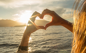 Young woman by the lake making a heart shape finger frame. Lake and mountain landscape.