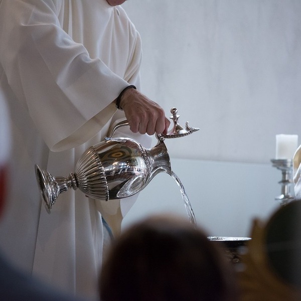 Pfarrer schüttet Weihwasser in das Becken
