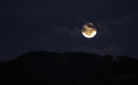 Der wolkenverhangene Mond geht des Nachts über einem Berg auf.