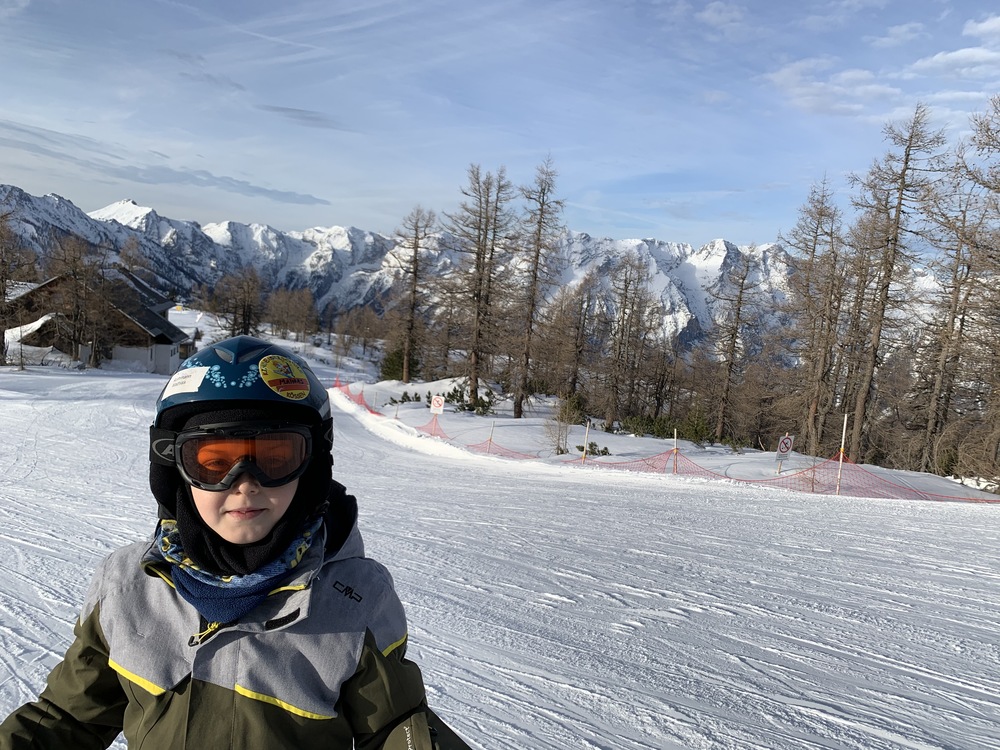 Kind in Skikleidung vor einer noch leeren Piste