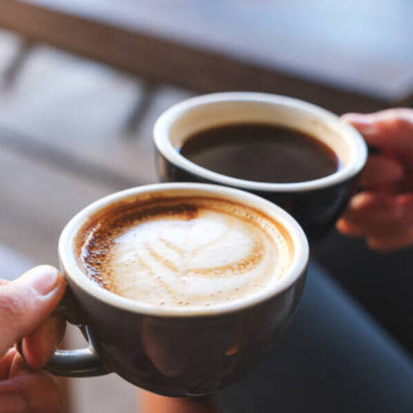 Closeup image of a man and a woman clinking white coffee mugs in cafe