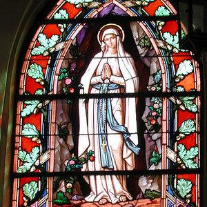 Leuchtendes Kirchenfenster. Darauf abgebildet: Maria mit weißem Gewand.
