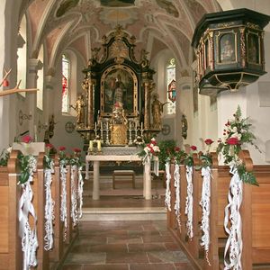 Blick in den Innenraum der Kirche. Kirchenbänke dekoriert mit jeweils einer Rose und weißer Schleife.