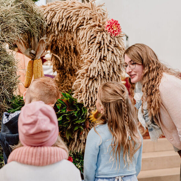 Tamara Rennleithner, Leiterin des Pfarrcaritas-Kindergartens und der Pfarrcaritas-Krabbelstube in Pichl bei Wels, zeigt den Kindern die Erntekrone in der Kirche.