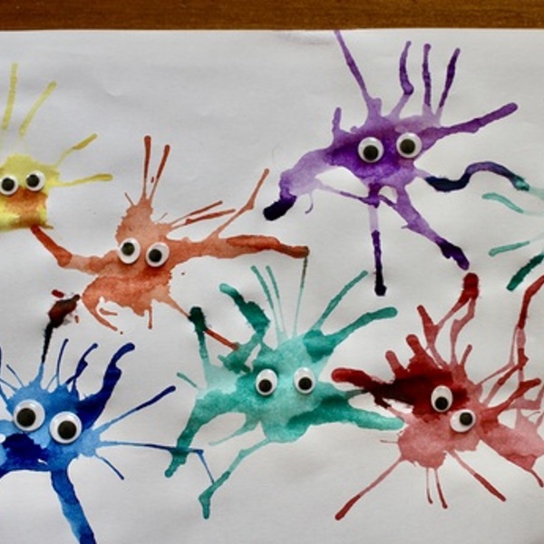 weißes Blatt Papier mit bunten Spritzflecken die mit Wackelaugen verziert sind 