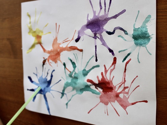 weißes Blatt Papier mit Farbspritz welche mit einem Strohhalm verblasen werden