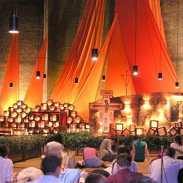 am Boden sitzende betende Menschen, Mann mit Gitarre, Kirche mit orangen Tüchern, viele Kerzen