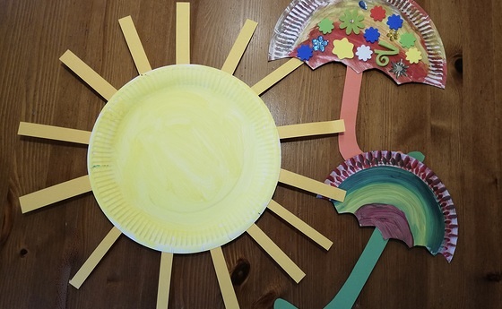 aus Papier ausgeschnittene Sonne mit zwei Regenschirmen die wie ein Regenbogen aussehene