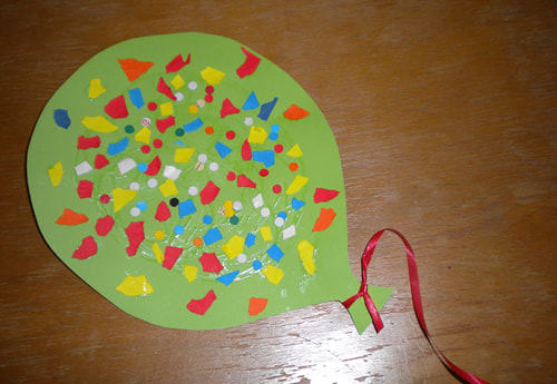 Luftballon aus grünen Papier ausgeschnitten, mit einer roten Schnur, mit bunten Blumen beklebt 