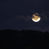 Der wolkenverhangene Mond geht des Nachts über einem Berg auf.